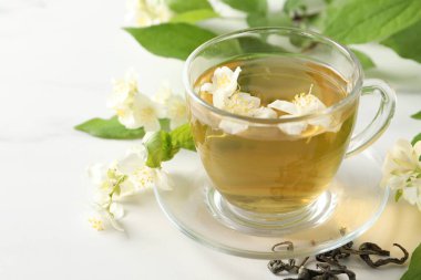 Aromatik yasemin çayı fincanda, çiçekler ve yapraklar beyaz masada