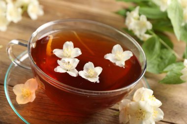 Sıcak yasemin çayı fincanda ve çiçekler ahşap masada, yakın plan.