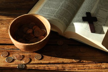 Bağış yap ve konsept ver. Tahta masada bozuk para, haç ve incil var.