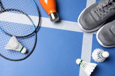 Tüylü badminton mekikleri, raketler, spor ayakkabıları ve şişeler sahada, düz yerde. Metin için boşluk