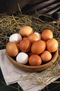 Kâsede taze tavuk yumurtası ve siyah ahşap masada kurutulmuş saman.