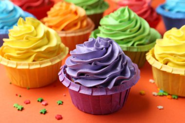 Delicious bright cupcakes and sprinkles on coral background, closeup