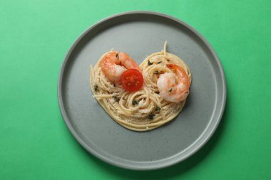 Yeşil arka planda lezzetli spagetti, domates, karides ve peynirden yapılmış bir kalp.