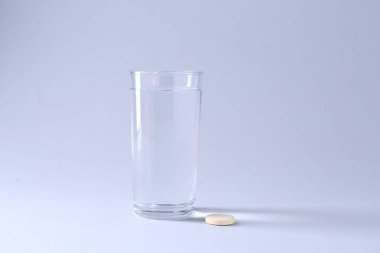 Fışkırtıcı hap ve açık gri arka planda bir bardak su.