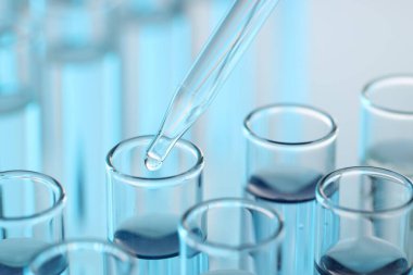 Işık arka planında pipetten test tüpüne sıvı damlatılıyor, yakın plan