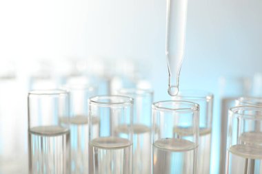 Işık arka planında pipetten test tüpüne sıvı damlatılıyor, yakın plan