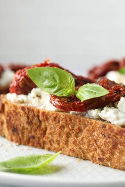 Lezzetli ricotta bruschetta, güneşte kurutulmuş domates ve tabakta fesleğen, yakın plan.