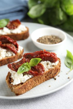 Lezzetli ricotta bruschettalar, güneşte kurutulmuş domatesler, fesleğen ve öğütülmüş biber, yakın plan.