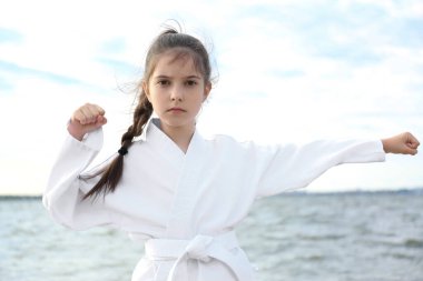 Kimonolu tatlı küçük kız nehir kenarında karate yapıyor.