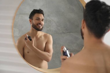 Adam evin içinde aynanın yanına lüks parfüm sıkıyor.