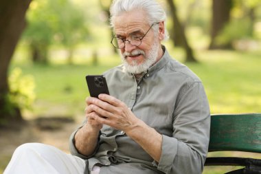 Parktaki bankta akıllı telefon kullanan mutlu büyükbabanın portresi.