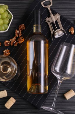 Kanat tirbuşonu, şarap şişesi, bardaklar, mantarlar, cevizler ve üzümler siyah masada, üst manzara