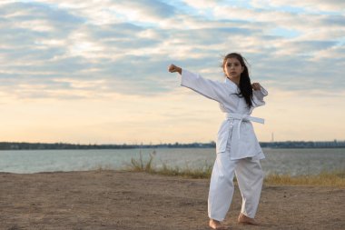 Kimonolu tatlı küçük kız nehir kenarında karate yapıyor.