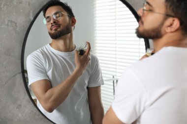 Adam evin içinde aynanın yanına lüks parfüm sıkıyor.