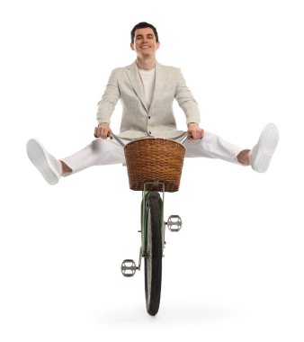 Gülen adam beyaz arka planda sepetle bisiklet sürerken eğleniyor.