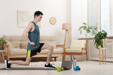 Çevrimiçi fitness eğitmeni. Evde dizüstü bilgisayar başında egzersiz yapan bir adam.