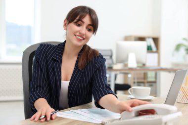 Smiling secretary taking telephone handset at table in office