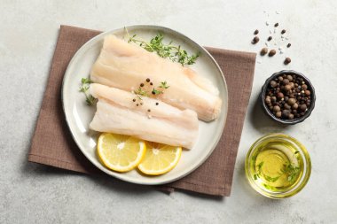 Çiğ morina balığı, baharat, mikro yeşillik ve limon tabağı gri desenli masada, düz yerde.