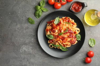 Domates soslu lezzetli makarna, fesleğen ve gri desenli masa üzerindeki ürünler, düz yatak. Metin için boşluk