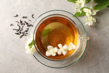 Aromatik yasemin çayı fincanda, çiçekler ve yapraklar açık gri masada, üst manzara