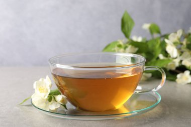 Aromatik yasemin çayı fincanda, çiçekler ve yeşil yapraklar açık gri masada