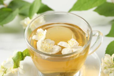 Aromatik yasemin çayı fincanda, çiçekler ve yeşil yapraklar masada, yakın çekim