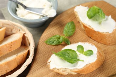 Krem peynirli ve fesleğenli lezzetli sandviçler ahşap masada, yakın plan.