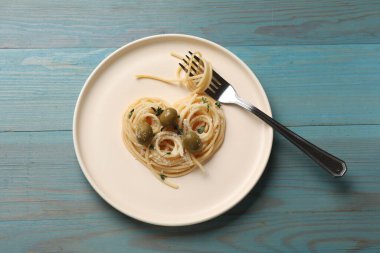 Nefis spagetti, çatal, zeytin ve peynirden yapılmış kalp açık mavi ahşap masa, üst manzara