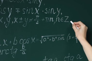 Teacher writing down math equation on green board, closeup