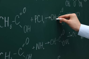 Teacher writing chemical formulas with chalk on green chalkboard, closeup