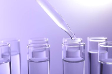 Pipetten menekşe arkaplanındaki test tüpüne sıvı damlatılıyor, yakın plan