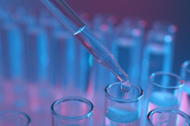 Renk arka planında pipetten test tüpüne sıvı damlatılıyor, yakın plan