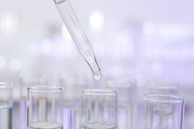 Işık arka planında pipetten test tüpüne sıvı damlatılıyor, yakın plan