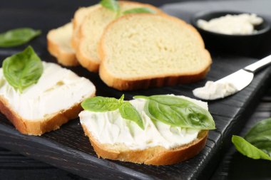 Krem peynirli ve fesleğenli ekmek parçaları siyah masada, yakın plan.