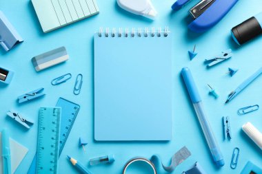 Açık mavi arkaplanda dizüstü bilgisayar, zımba ve farklı kırtasiye malzemesi ile düz konum