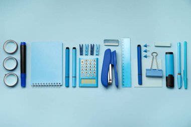 Açık mavi arkaplanda dizüstü bilgisayar, zımba ve farklı kırtasiye malzemesi ile düz konum