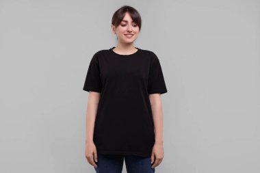 Siyah tişörtlü, açık gri arka planda gülümseyen kadın.