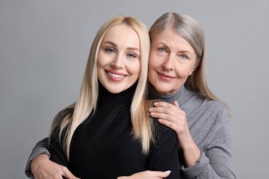 Family portrait of young woman and her mother on grey background