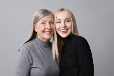 Family portrait of young woman and her mother on grey background