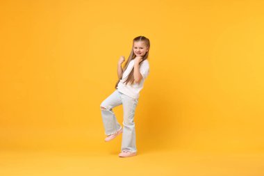 Sarı arka planda dans eden tatlı küçük kız, mesaj için yer var.