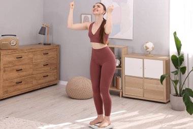 Happy woman standing on floor scale at home