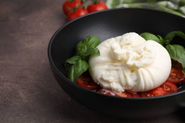 Lezzetli burrata peyniri, domates ve fesleğen kahverengi masada, yakın plan.