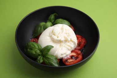 Lezzetli burrata peyniri, domates ve fesleğen yeşil masada, yakın plan.