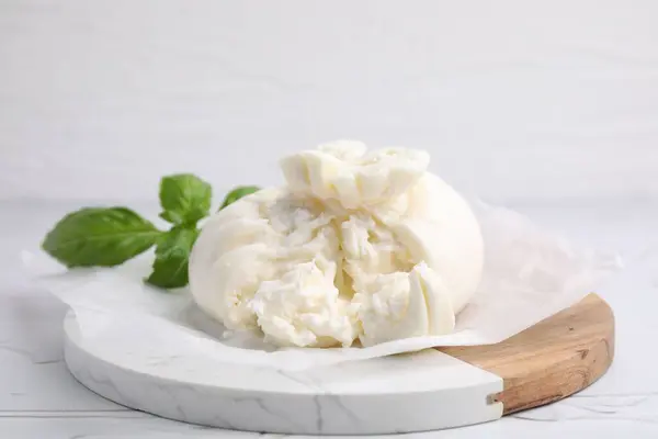 stock image Delicious fresh burrata cheese with basil leaves on white textured table, closeup