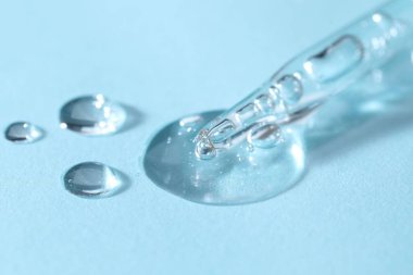 Açık mavi arkaplanda cam pipet ve şeffaf sıvı, yakın plan.