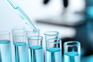 Bulanık arkaplanda pipetten test tüpüne sıvı damlatılıyor.