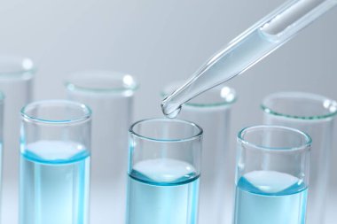 Işık arka planında pipetten test tüpüne sıvı damlatılıyor, yakın plan