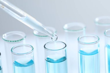 Işık arka planında pipetten test tüpüne sıvı damlatılıyor, yakın plan