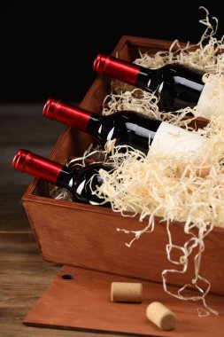 Ahşap masanın üzerinde şarap şişeleri olan bir kutu.