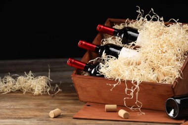 Siyah arka planda ahşap masada şarap şişeleri olan bir kutu. Metin için boşluk